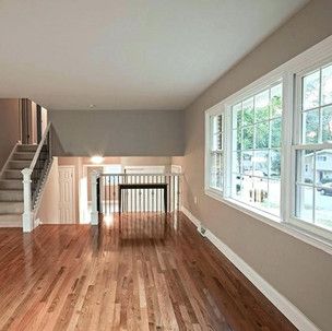 An empty living room with hardwood floors , stairs , and lots of windows.