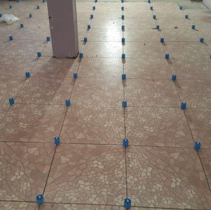 A tiled floor with blue plastic spacers on it.