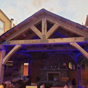 A wooden gazebo with blue lights on it and a fireplace.