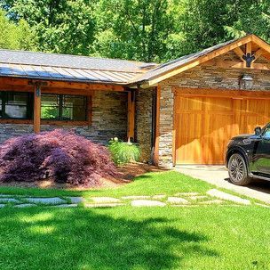 A car is parked in front of a house with a wooden garage door.
