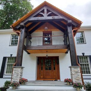 The front of a white house with a wooden porch and balcony.