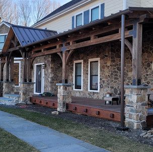 A large stone house with a wooden porch and a metal roof.