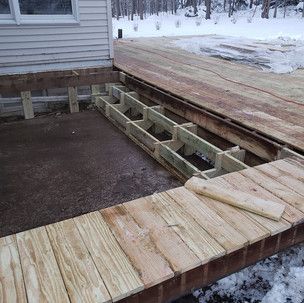 A wooden deck is being built next to a house in the snow.