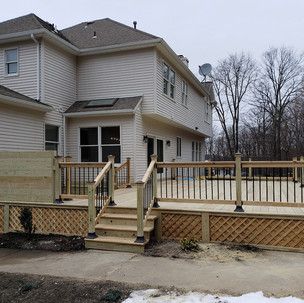 A large white house with a wooden deck and stairs in front of it.