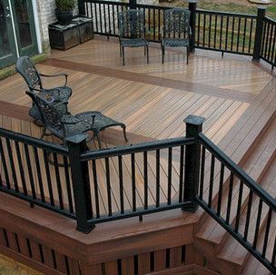 A wooden deck with a black railing and chairs.