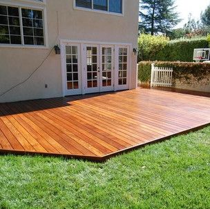 A large wooden deck is sitting on top of a lush green lawn in front of a house.