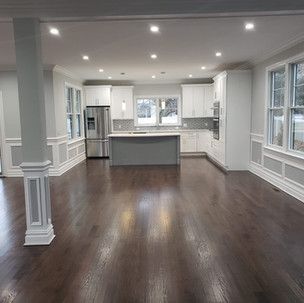 A kitchen with hardwood floors , white cabinets , stainless steel appliances , and a large island.