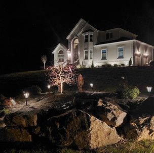 A large white house is lit up at night with rocks in front of it.