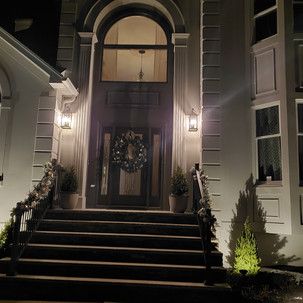 The front door of a house with a wreath on it is lit up at night.