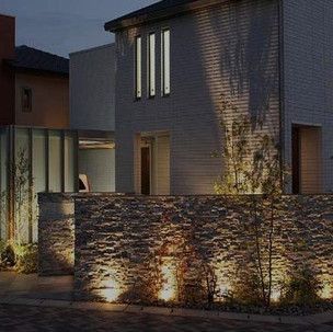 A house with a stone wall in front of it is lit up at night.