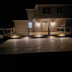 A house with a deck and stairs is lit up at night.
