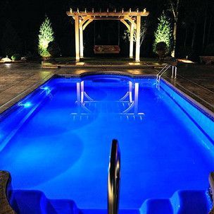 A large swimming pool is lit up at night with blue lights.