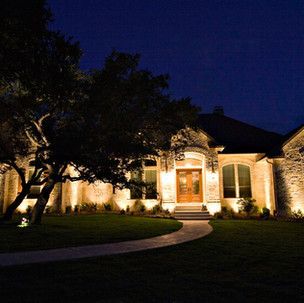 A large house is lit up at night with trees in front of it.