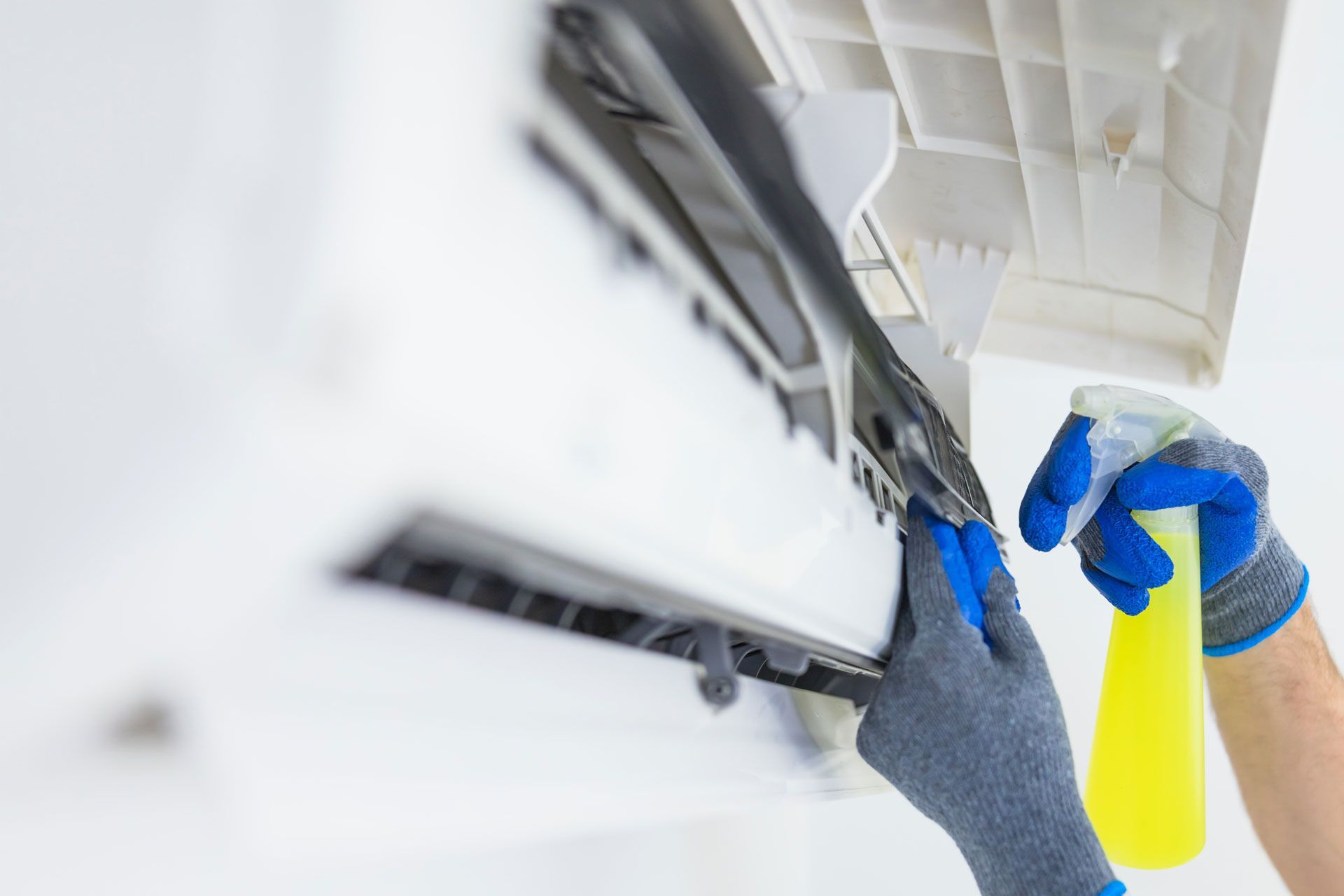 A person is cleaning an air conditioner with a spray bottle.