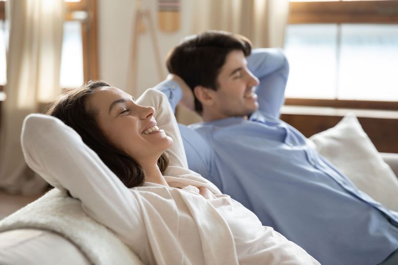 Two people reclining on sofas in a bright room, smiling with eyes closed and arms behind their heads
