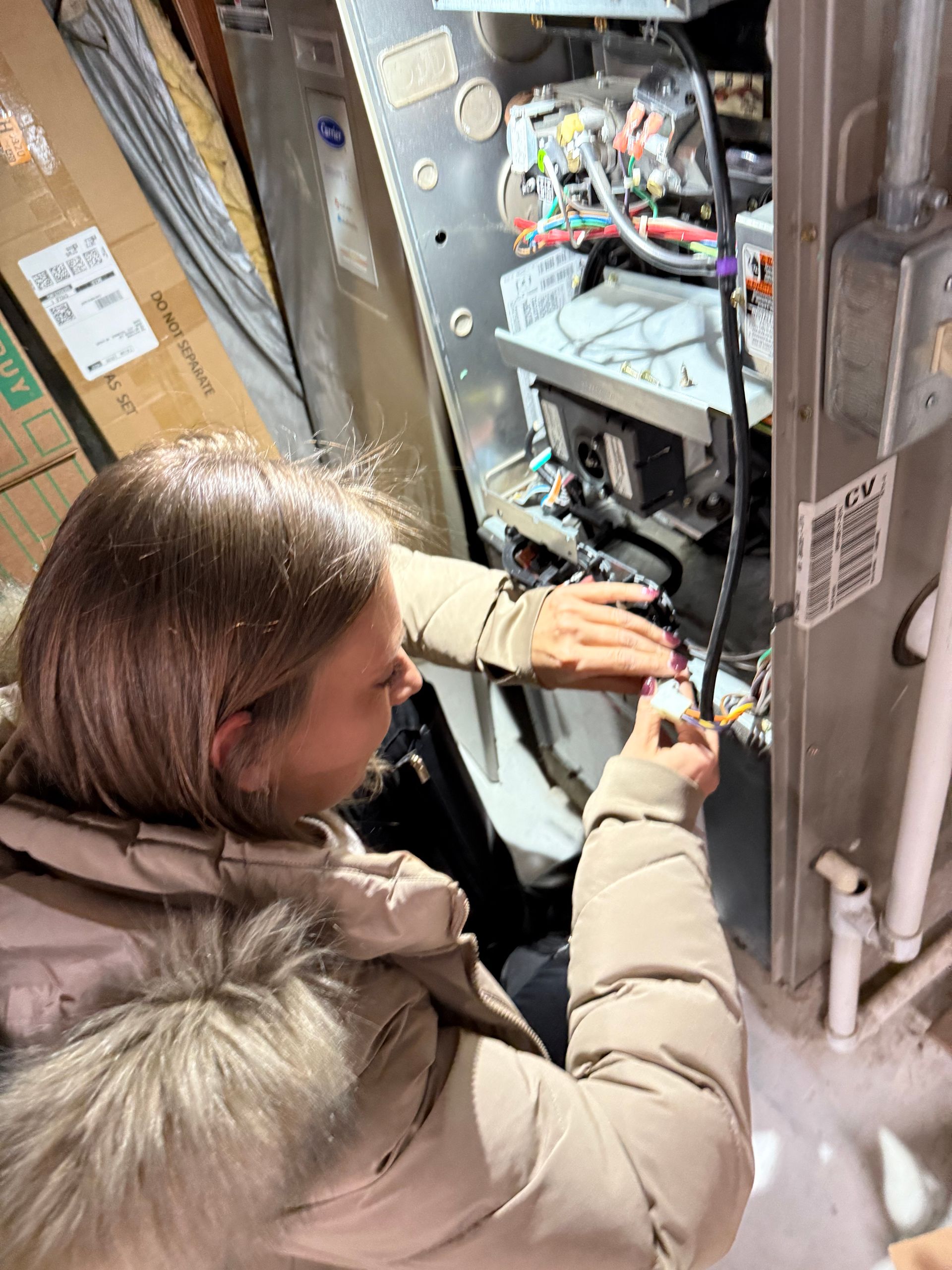 A woman is working on an air conditioner in a basement.
