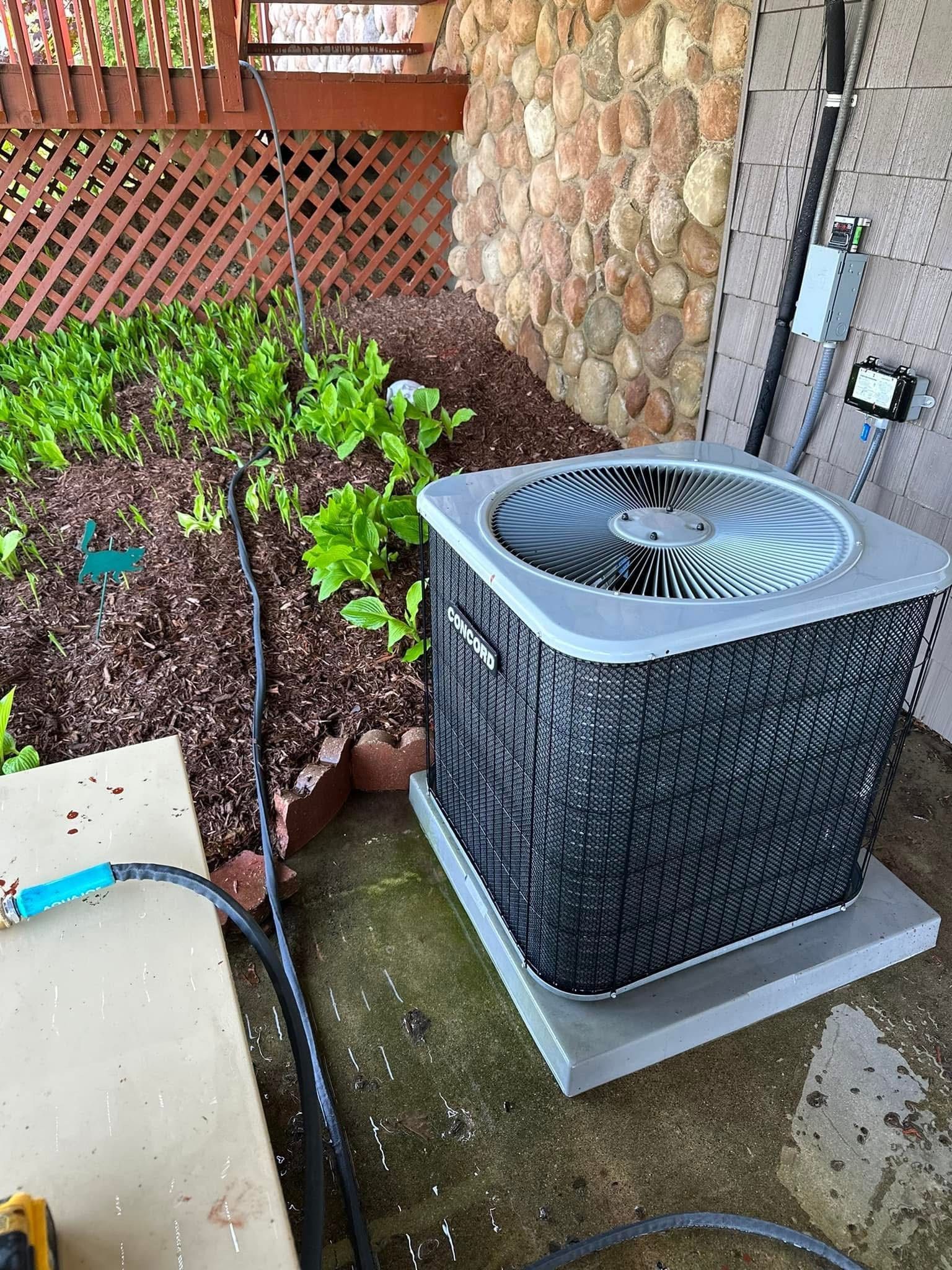 An air conditioner is sitting on the sidewalk next to a garden.