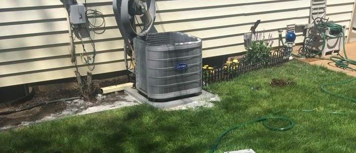 An air conditioner is sitting in the grass in front of a house.