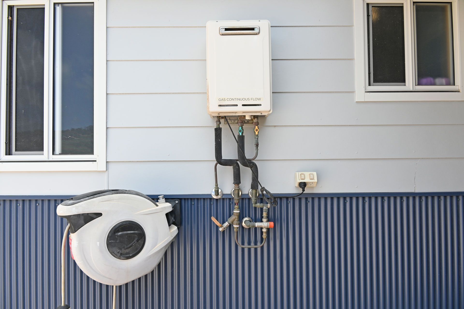 A white water heater is attached to the side of a house