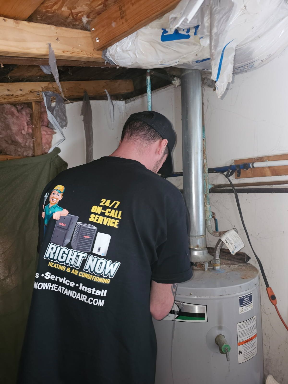 A man wearing a right now shirt is working on a water heater
