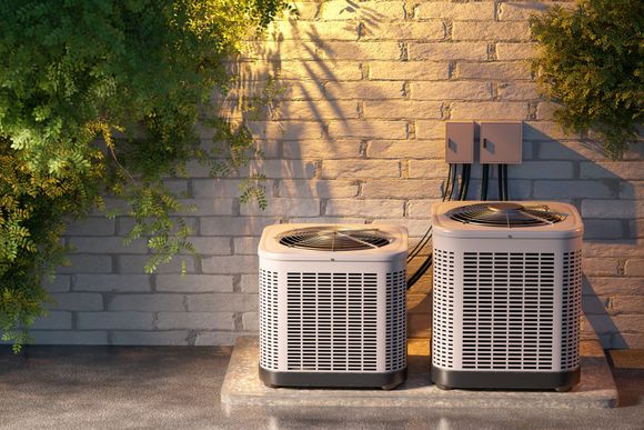 Two outdoor air conditioning units beside a brick wall with ivy in warm sunlight