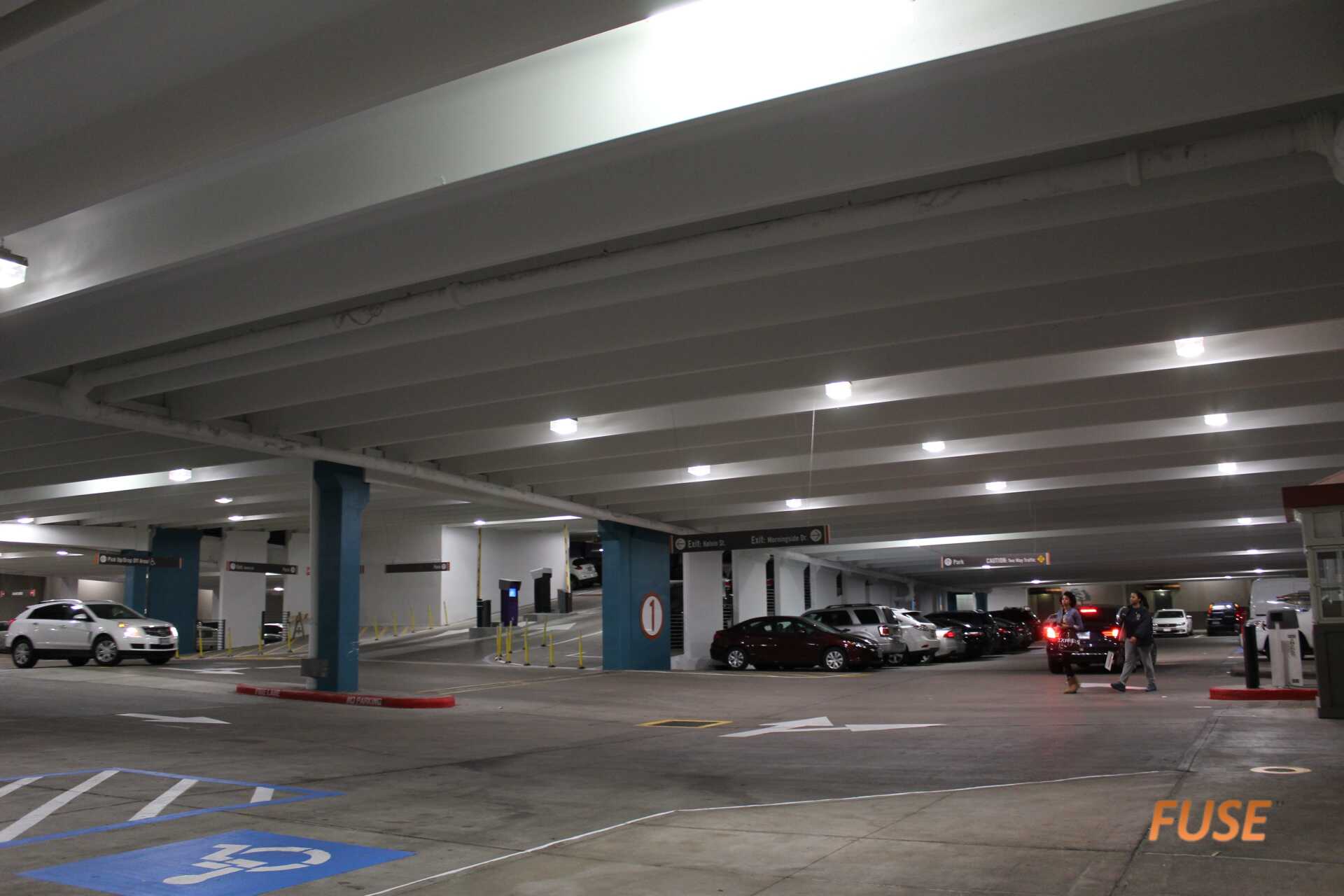 A parking garage with cars parked in it and people walking around.