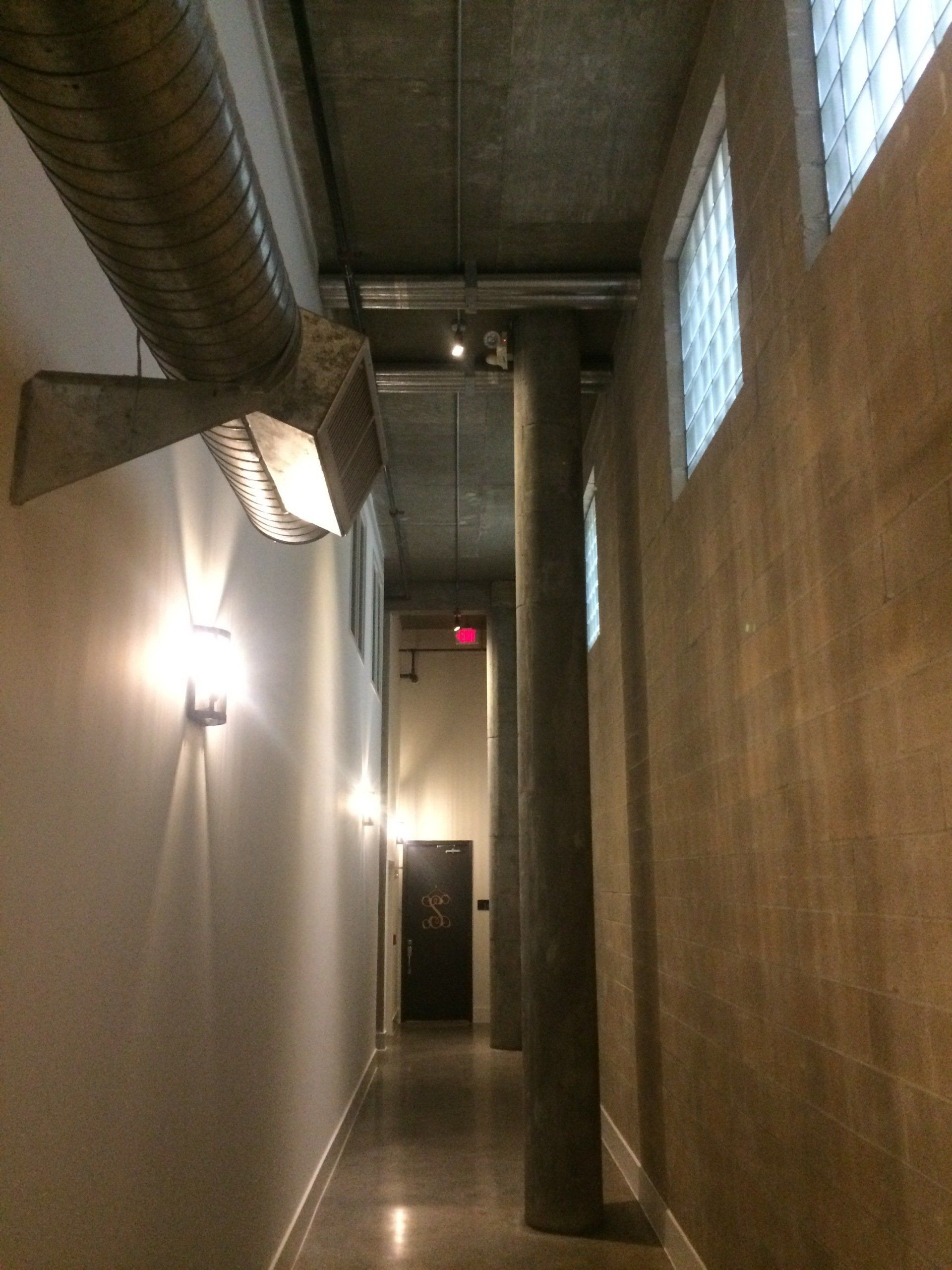 A long hallway with columns and a red exit sign