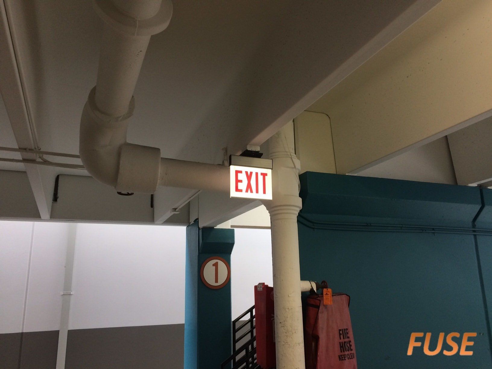 An exit sign is hanging from the ceiling of a building.