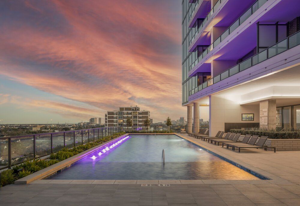 A large swimming pool is surrounded by chairs and a building at sunset.