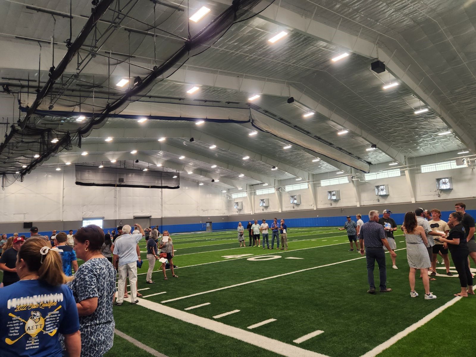 A group of people are standing on a football field in an indoor stadium.