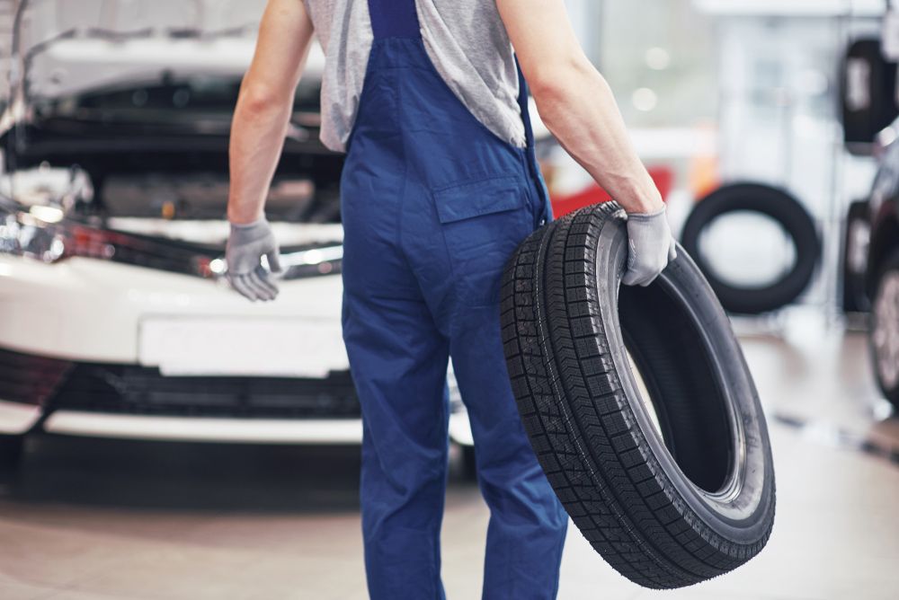 A Mechanic Is Holding a Tire in Front of A Car — Rasmussen Mechanical & Tyres in Garbutt, QLD