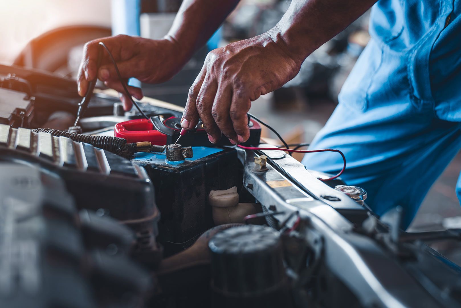 A Man Is Working on A Car Battery in A Garage — Rasmussen Mechanical & Tyres in Garbutt, QLD
