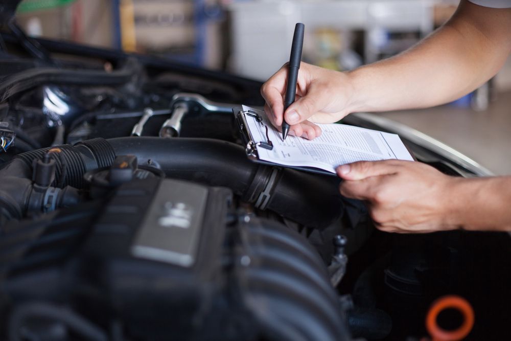 A Person Is Writing on A Clipboard Under the Hood of A Car — Rasmussen Mechanical & Tyres in Garbutt, QLD