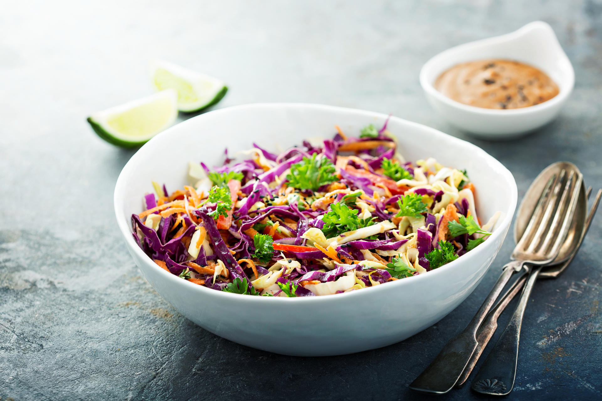 A bowl of coleslaw with carrots , cabbage and parsley on a table.