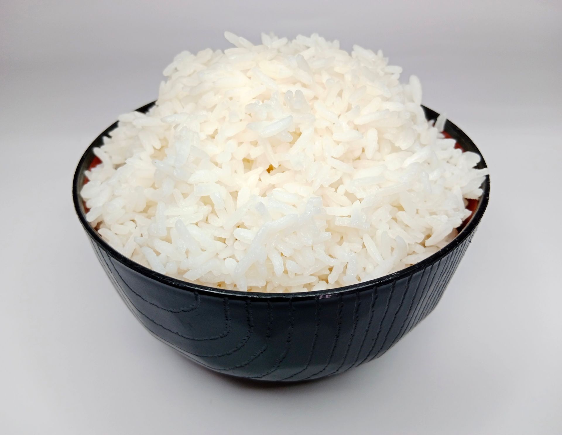 A black bowl filled with white rice on a white background