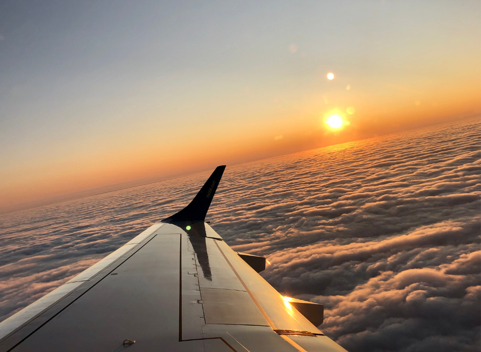 The wing of an airplane flying over the clouds at sunset