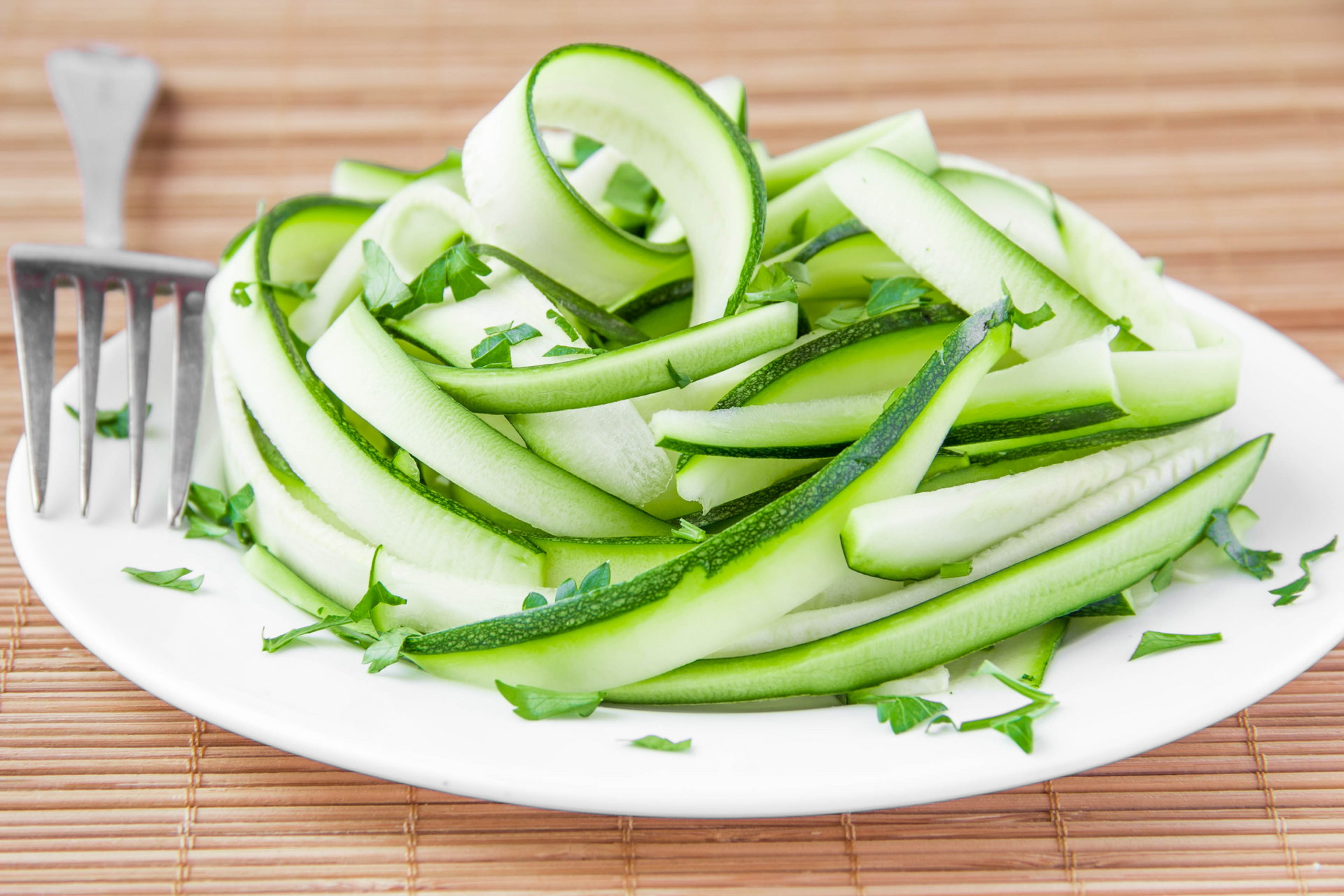 A white plate topped with sliced zucchini and a fork.