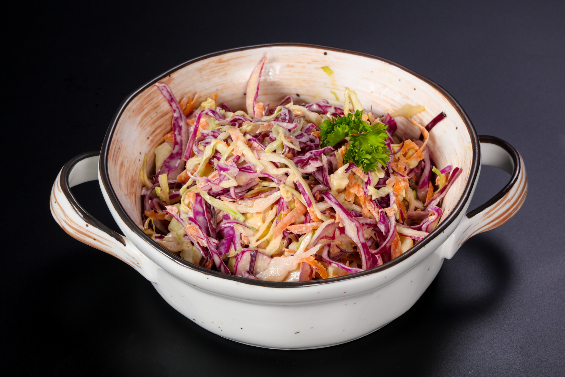 A white bowl filled with coleslaw on a black table.