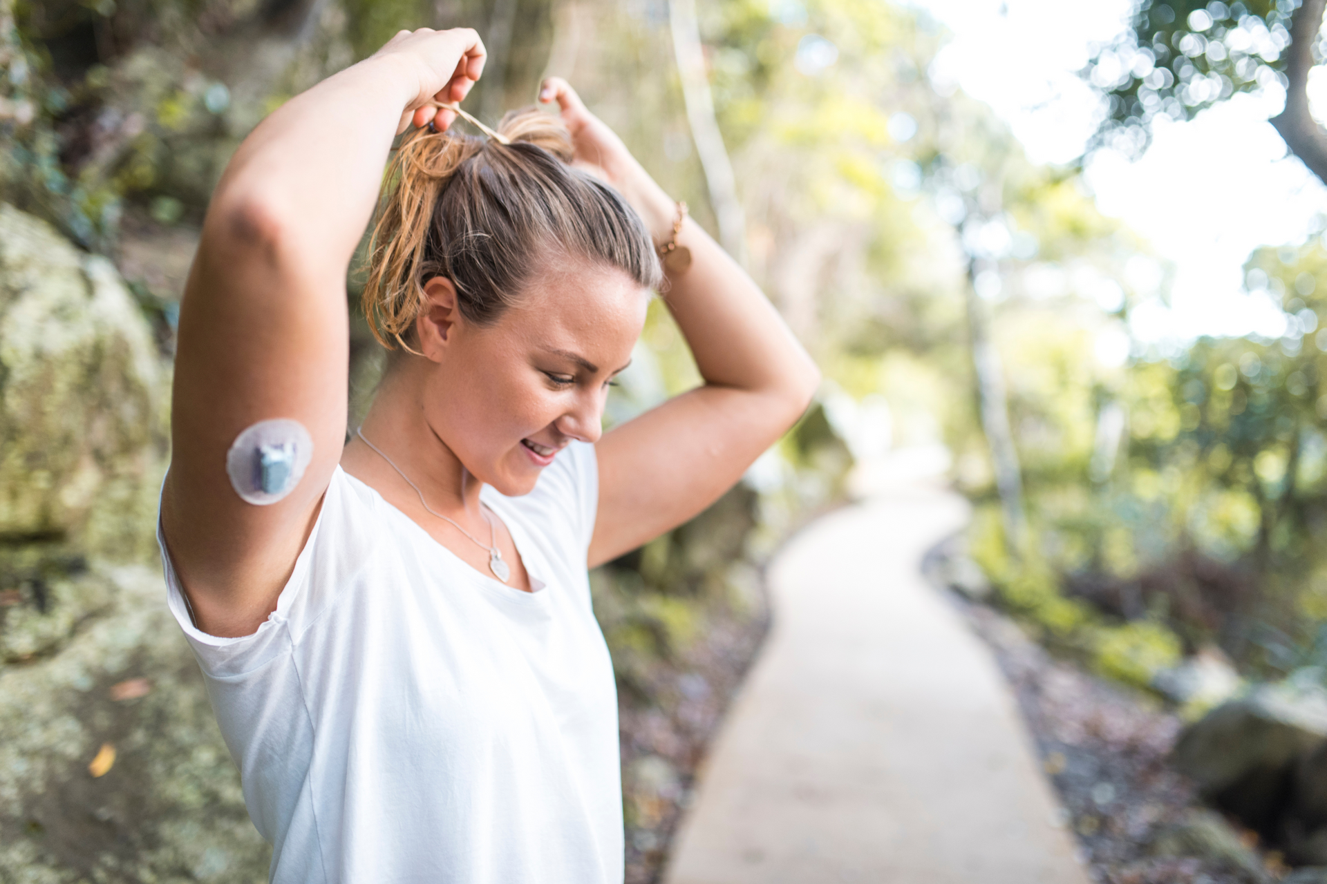 A woman with a diabetes patch on her arm is putting her hair in a ponytail.