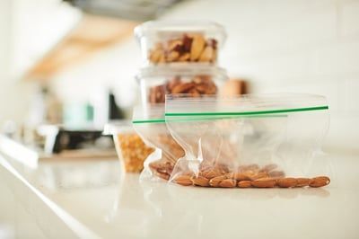 A bag of almonds is sitting on a counter next to a stack of plastic containers.