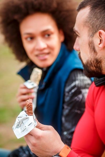 A man and a woman are sitting on a bench eating ice cream bars.