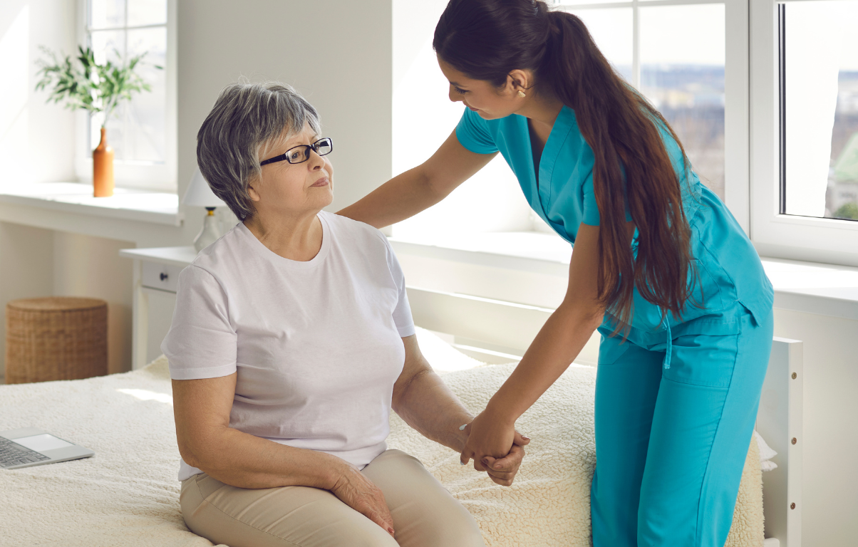 A caregiver assisting an elderly woman by holding her hand, illustrating compassionate care and support for seniors in a home environment.