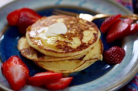 A stack of pancakes with syrup and strawberries on a blue plate.