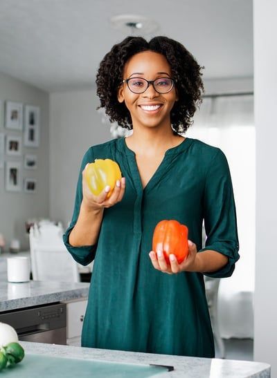 A woman is holding two peppers in her hands in a kitchen.