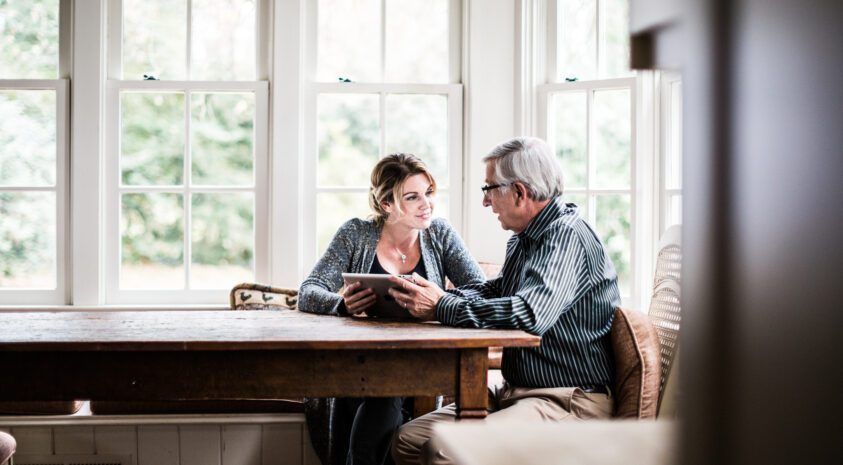 A man and a woman are sitting at a table looking at a tablet.