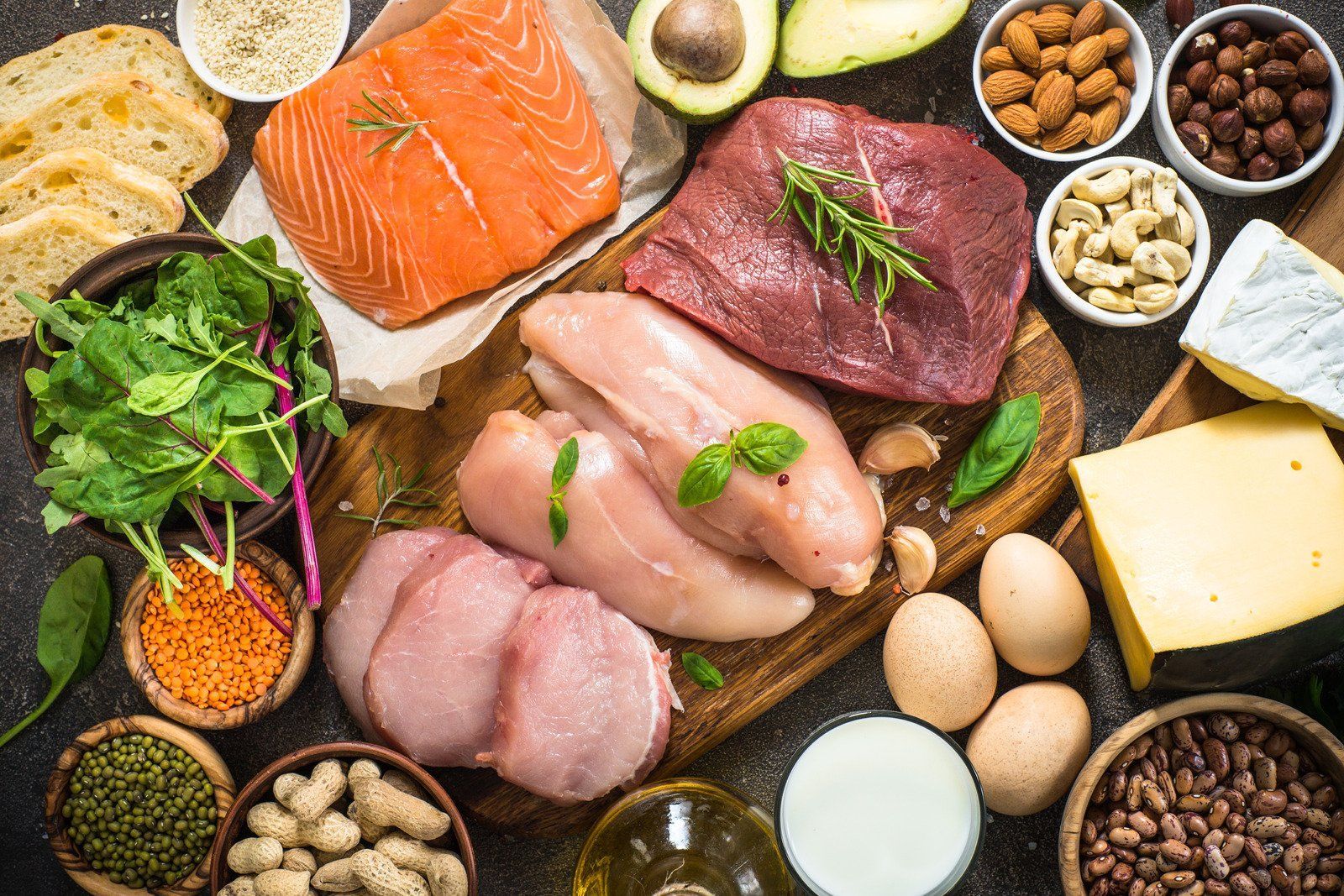Assortment of high-protein foods: salmon, steak, chicken, eggs, nuts, cheese, lentils, and vegetables.