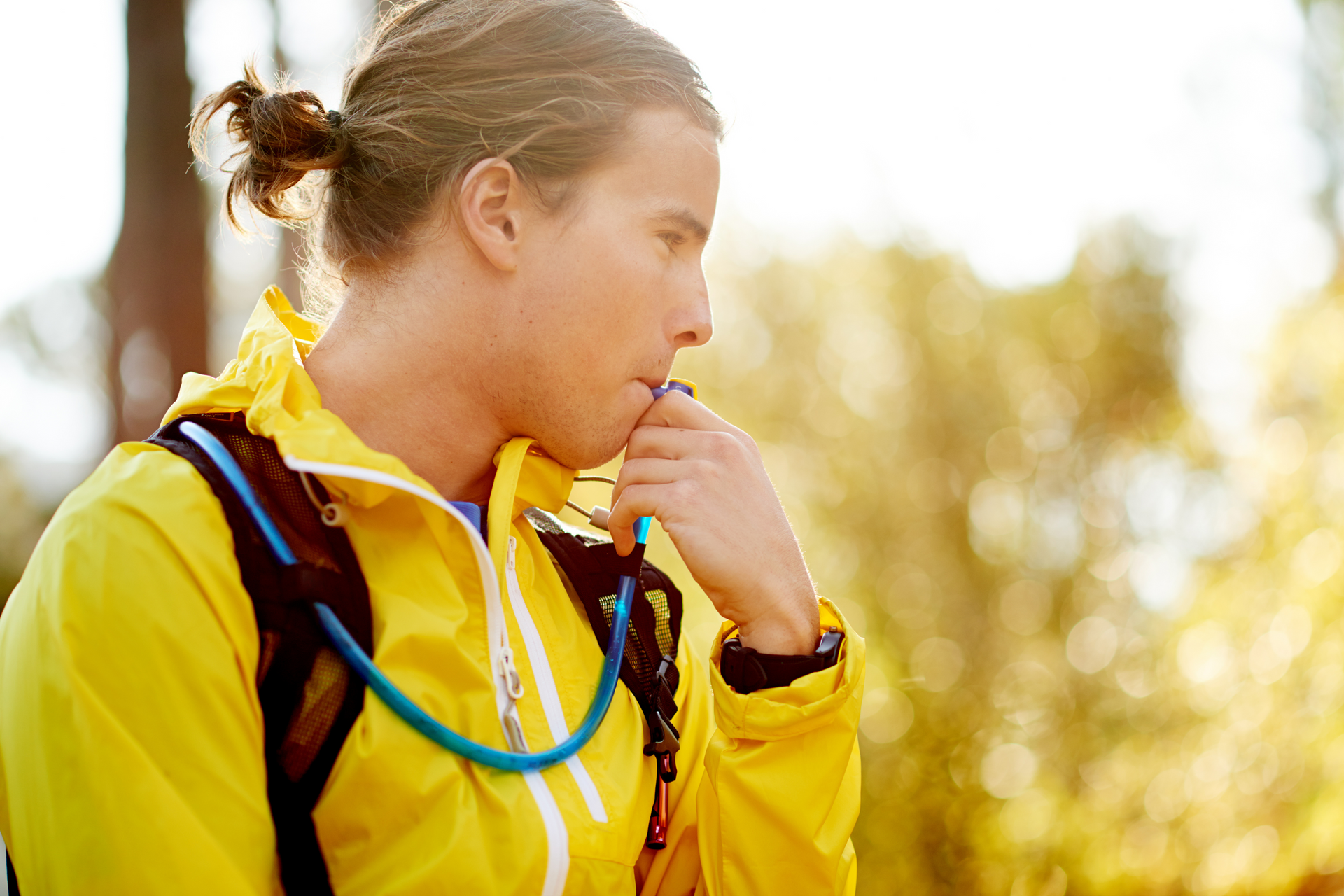 A man in a yellow jacket is drinking water from a water bottle.