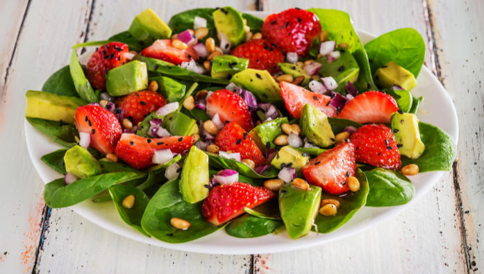 A salad with spinach , strawberries , avocado and pine nuts on a white plate.