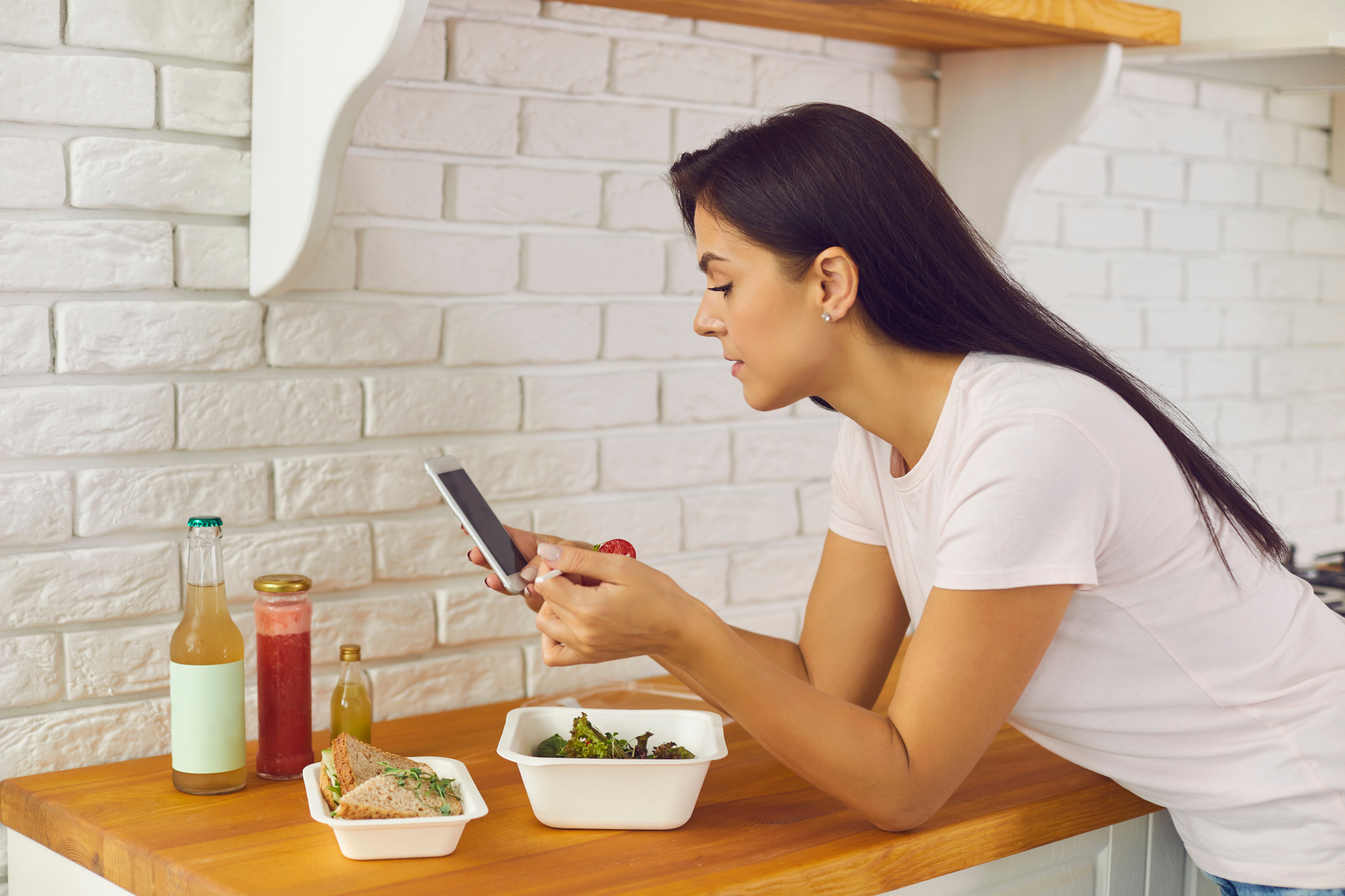 A woman is sitting at a kitchen counter looking at her cell phone.