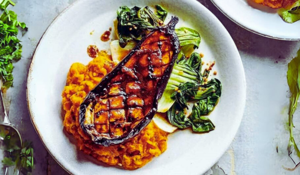 A white plate topped with a grilled eggplant and vegetables.